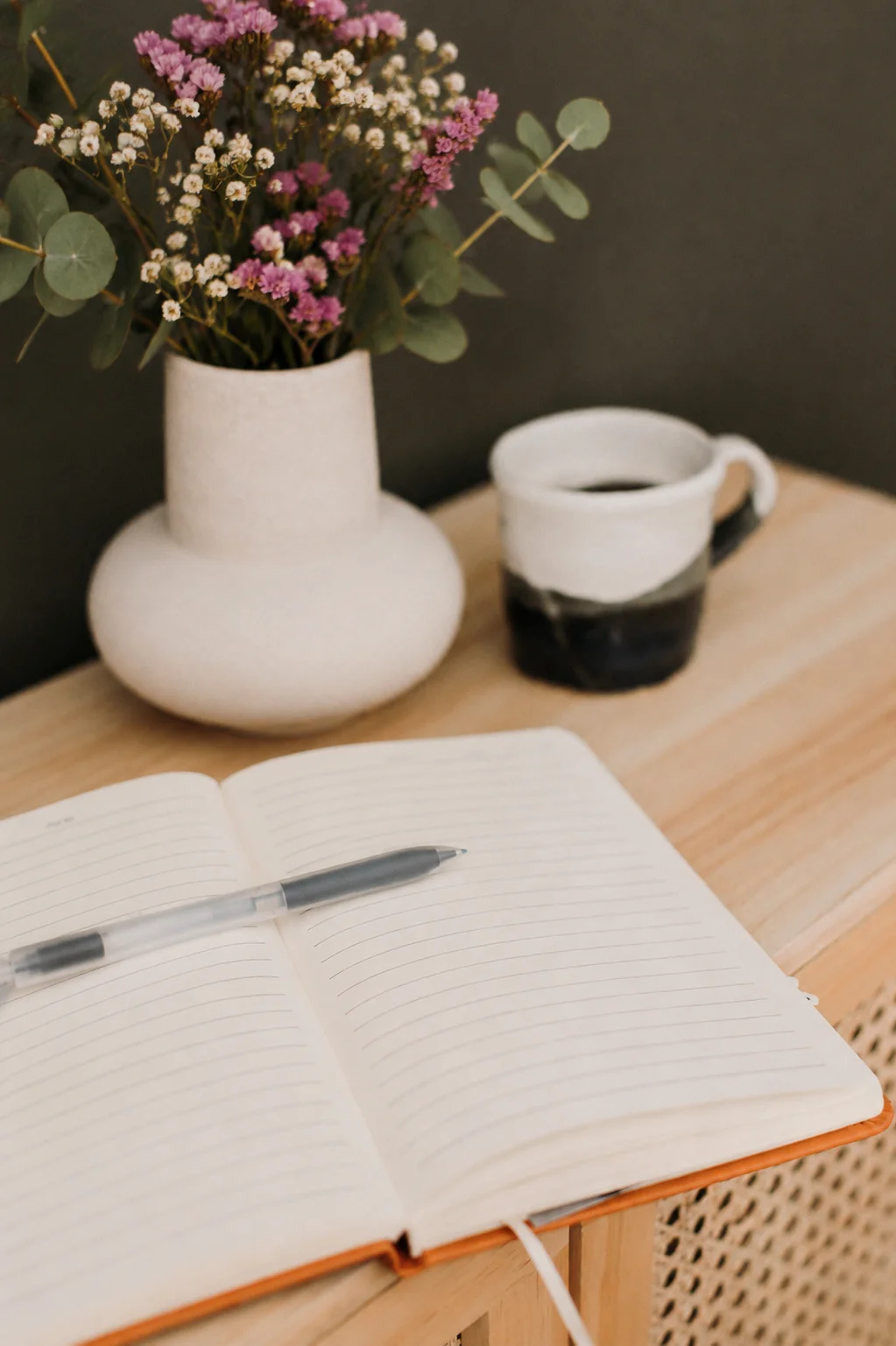 Cuaderno abierto sobre una mesa de madera junto a una taza y flores secas en un ambiente cálido y tranquilo.